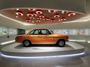 Pomarańczowy samochód BMW 2002 TI w muzealnej scenografii